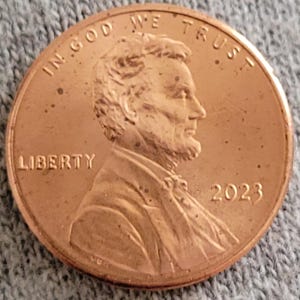 May include: A close-up of a copper-colored United States penny. The coin features the profile of Abraham Lincoln, the word "LIBERTY", the year "2023", and the phrase "IN GOD WE TRUST".