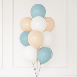 May include: A cluster of pastel-colored balloons, including blue, white, and beige, tied together. Below, a white table displays a banner that spells "ONE", a party hat, and wooden beads. The balloons are a festive decoration.
