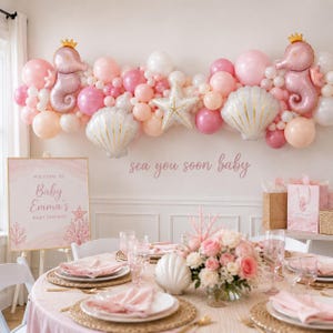 Może przedstawiać: Dekoracja na baby shower z łukiem z różowych i białych balonów oraz balonami foliowymi w kształcie koników morskich, muszli i rozgwiazd. Tabliczka zawiera napis Welcome to Baby Emma's Baby Shower oraz sea you soon baby.