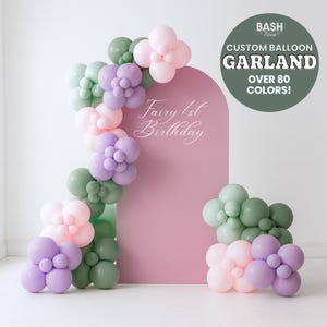 Puede incluir: Una guirnalda de globos en colores pastel decora un arco rosa, con el texto "Fairy 1st Birthday". Un círculo verde dice "Custom Balloon Garland, Over 80 Colors!"
