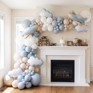 May include: A balloon arch featuring white, beige, and light blue balloons with foil airplane and cloud balloons. The display includes a cake with a number one topper, vintage-style suitcases, model airplanes, and a sign that reads TIME FLIES.