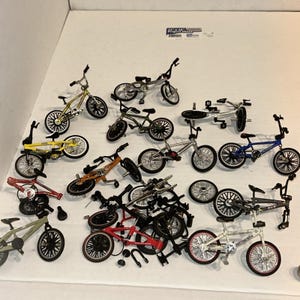 May include: A selection of miniature BMX bikes in various colours, including yellow, green, red, and silver. The bikes have detailed features like handlebars, seats, and wheels. Some bikes are complete, while others are disassembled.