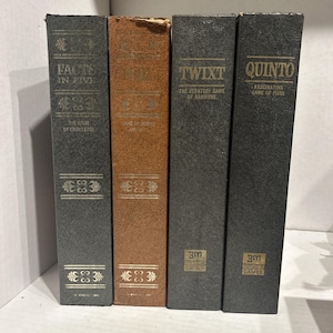 Könnte beinhalten: Vier Vintage-Brettspiele in einer Reihe. Die Spiele befinden sich in dunkelgrauen und braunen Boxen mit goldfarbenen Buchstaben. Zu den Titeln gehören "Facts in Five", "Othello", "Twixt" und "Quinto". Die Spiele "Twixt" und "Quinto" haben das Logo "3M Bookshelf Games".