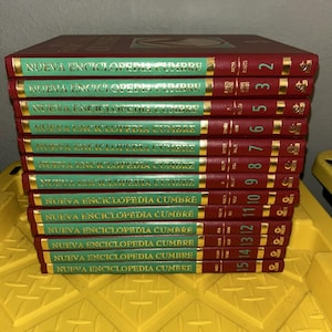 May include: A stack of red hardcover books with gold lettering and green spines. The text "NUEVA ENCICLOPEDIA CUMBRE" is visible on the spines. Numbers 2 to 15 are visible on the spines. The books are stacked on a yellow surface.