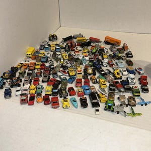 May include: A large collection of assorted miniature die-cast toy vehicles, including various cars, trucks, emergency vehicles, and aircraft in a wide array of colors such as red, blue, yellow, green, black, and white, scattered across a flat surface.