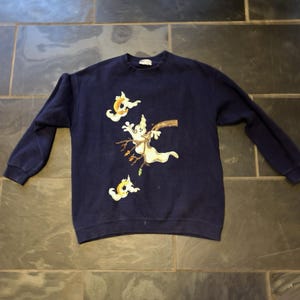 May include: A navy blue long-sleeve sweatshirt featuring a graphic print of three white ghosts. One ghost is perched on a brown tree branch, while the other two smaller ghosts are positioned above and below, each holding a yellow crescent moon.