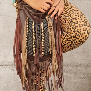 May include: A dark brown leather drawstring bag featuring long fringe accents in both dark brown and tan. The front panel is decorated with vertical rows of black cylindrical beads interspersed with small light-colored wooden beads.
