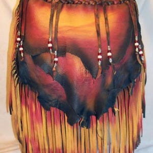 May include: A leather shoulder bag featuring a gradient of red, orange, and black colors. The bag has a braided top edge with hanging leather strips adorned with small white and red beads. The bottom section consists of long, thin leather fringe.