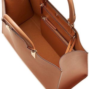 Può includere: Una borsa tote in pelle marrone chiaro con un design strutturato. La borsa presenta due manici, una piccola tasca interna con cerniera e dettagli hardware color oro. L'interno è anch'esso marrone chiaro.
