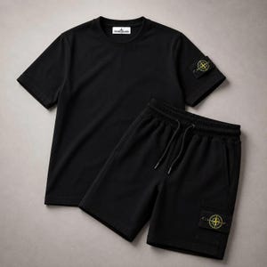 Op de afbeelding: Een zwart T-shirt met korte mouwen en ronde hals en een bijpassende zwarte korte broek. Het T-shirt heeft een Stone Island-label in de nek en een kompas-patch op de linkermouw. De korte broek heeft een elastische tailleband met trekkoorden en een kompas-patch op de linkerbeenzak.
