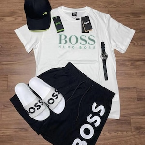 May include: A collection of men's apparel including a white t-shirt, black shorts, a black baseball cap, and white sandals. The t-shirt and shorts feature the word "BOSS" in large lettering. A black wristwatch is also included.