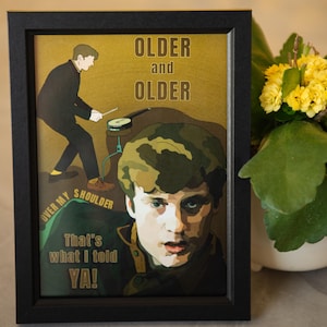 May include: Framed art print with a vintage-style illustration. The artwork features a man playing drums, with the text "OLDER and OLDER" and "OVER MY SHOULDER That's what I told YA!" in a retro font. The print is in a black frame.