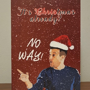 May include: A festive Christmas card with a red background and white speckles. The card reads "It's Christmas already?" and "NO WAY!" A man in a Santa hat and blue sweater is pointing to the left.
