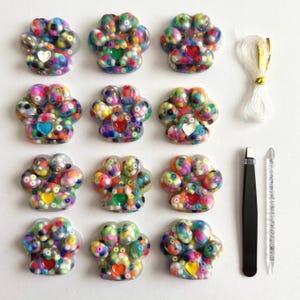 May include: Nine colorful paw-shaped resin embellishments with various heart-shaped accents. The embellishments are surrounded by small beads in a variety of colors. Also included are white thread, black tweezers, and a silver tool.