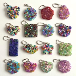 May include: A collection of colorful, beaded keychains in various shapes, including hearts, stars, and squares. Each keychain features a silver chain and a unique pattern of small, vibrant beads in shades of blue, green, red, and yellow.