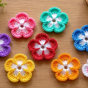 May include: A collection of eight crocheted flower appliques, each featuring five rounded petals with a white center. The flowers are crafted in vibrant colors including purple, pink, teal, red, blue, yellow, orange, and a white flower with pink tips.