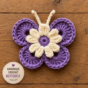 May include: A handmade crochet butterfly in shades of purple and cream. The butterfly features four circular wings in a deep purple, with a cream-coloured flower at the centre. The text "HANDMADE CROCHET BUTTERFLY" is on a round label.