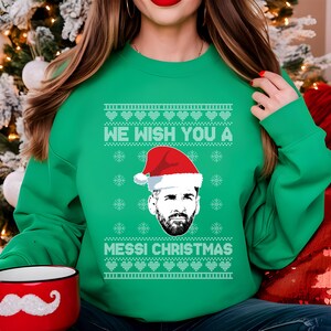 Puede incluir: Jersey navide&ntilde;o verde con el texto "WE WISH YOU A MESSI CHRISTMAS" y un gr&aacute;fico de Lionel Messi con un gorro de Pap&aacute; Noel. El jersey tiene un dise&ntilde;o festivo, perfecto para la temporada navide&ntilde;a.