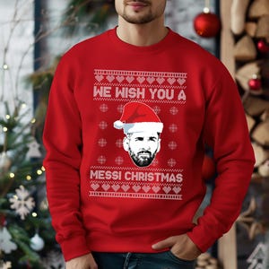 Puede incluir: Jersey navide&ntilde;o rojo con el texto "WE WISH YOU A MESSI CHRISTMAS" en blanco. El jersey presenta un gr&aacute;fico de una persona con un gorro de Pap&aacute; Noel. El jersey es un dise&ntilde;o festivo navide&ntilde;o.