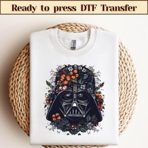 May include: White t-shirt featuring a black and white illustration of Darth Vader's helmet surrounded by colourful flowers.