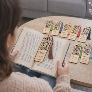 Op de afbeelding: Houten bladwijzers met ingewikkelde uitgesneden patronen en kleurrijke kwastjes. Eén bladwijzer ligt in een open boek, met de tekst "Merci pour ton amour". Verschillende andere bladwijzers liggen op een houten tafel.