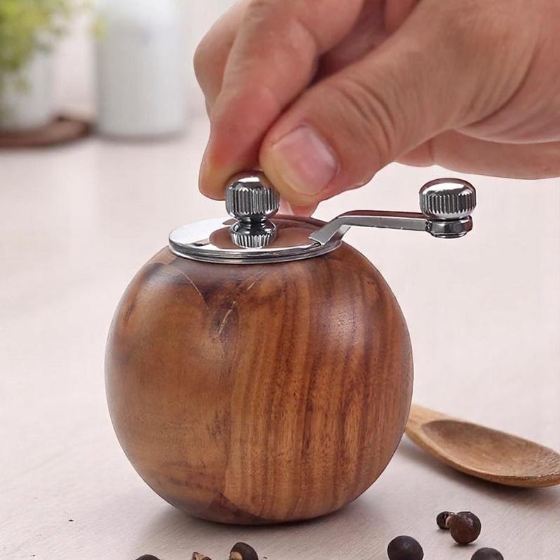 K&ouml;nnte beinhalten: Ein Pfefferm&uuml;hle aus Holz mit einem verchromten Oberteil und einem Kurbelgriff. Die M&uuml;hle ist rund und hat eine Holzmaserung.