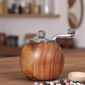 K&ouml;nnte beinhalten: Ein Pfefferm&uuml;hle aus Holz mit silbernem Deckel und Kurbel. Die M&uuml;hle ist rund und hat eine dunkelbraune Holzmaserung.