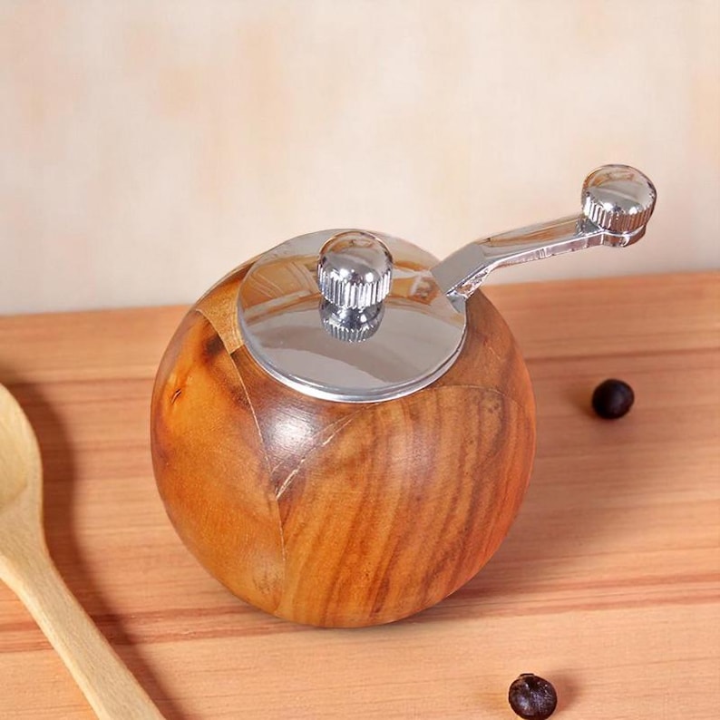 K&ouml;nnte beinhalten: Eine Pfefferm&uuml;hle aus Holz mit einem verchromten Deckel und Griff. Die M&uuml;hle ist rund und hat eine dunkelbraune Holzmaserung.