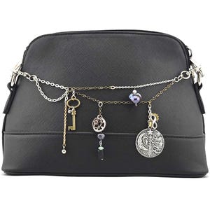 May include: Black dome-shaped handbag with a decorative chain. The chain features charms including a key, a gear, a coin, and beads. The bag has a textured surface and silver-tone hardware.