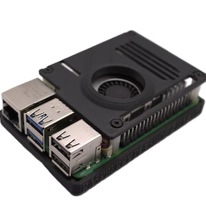 Peut inclure: Un ordinateur Raspberry Pi noir avec un ventilateur et un boîtier noirs. L'ordinateur dispose de plusieurs ports USB et d'un port Ethernet. Le boîtier présente un design texturé.