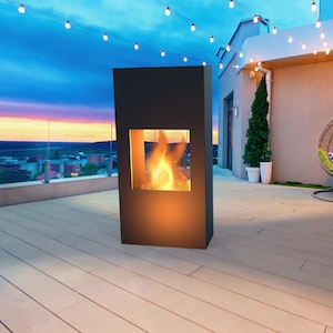 Könnte beinhalten: Ein moderner, schwarzer Außenkamin mit rechteckigem Design. Der Kamin hat ein Glasfenster, das eine hellorange Flamme zeigt. Die Szene spielt sich auf einer Dachterrasse mit Skyline-Hintergrund und Lichterketten ab.