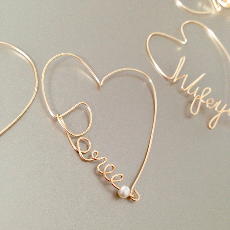 May include: Two gold wire heart-shaped ornaments with the names "Wifey" and "Darrel" spelled out in wire. The "Darrel" ornament has a small pearl at the bottom.