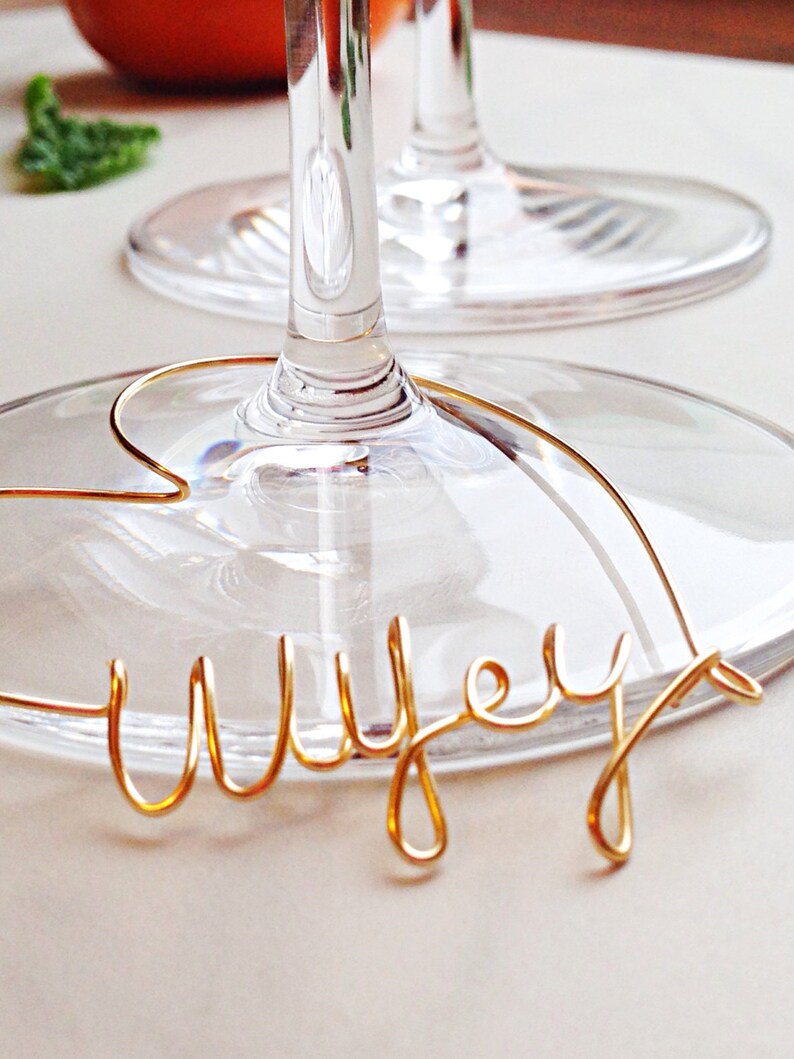 May include: A gold wire word "Wife" is wrapped around the stem of a clear wine glass.