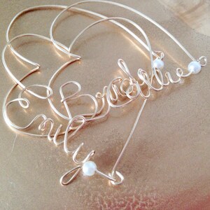 May include: Gold wire heart-shaped ornament with the names "Emily" and "Bradley" spelled out in wire. The ornament is decorated with small white pearls.