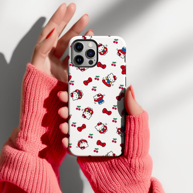 Może przedstawiać: Białe etui na telefon z powtarzającym się wzorem postaci Hello Kitty, czerwonych kokardek i wiśni. Etui ma błyszczące wykończenie i jest przeznaczone do smartfona. Projekt zawiera Hello Kitty w r&oacute;żnych strojach i pozach.