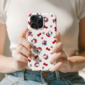 Może przedstawiać: Białe etui na telefon z powtarzającym się wzorem kresk&oacute;wkowego kota, czerwonych kokardek i wiśni. Kot ma na sobie czerwoną kokardkę i niebieski str&oacute;j. Etui ma błyszczące wykończenie i wycięcie na aparat.