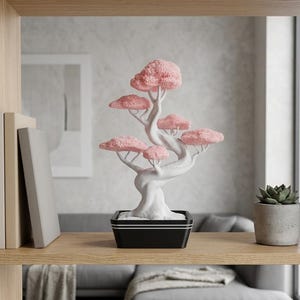 Könnte beinhalten: Ein dekorativer Bonsai-Baum mit weißem Stamm und Ästen, gekrönt von rosa, wolkenförmigem Laub. Der Baum steht in einem schwarzen, rechteckigen Topf mit weißer Umrandung, ausgestellt auf einem Holzregal. Eine kleine Sukkulente in einem grauen Topf befindet sich ebenfalls auf dem Regal.