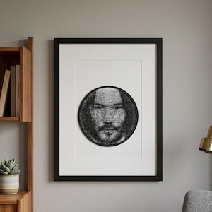 Könnte beinhalten: Ein gerahmtes Kunstwerk mit einem schwarz-weißen String-Art-Porträt eines Männergesichts. Das Kunstwerk befindet sich vor einem weißen Hintergrund in einem schwarzen Rahmen. Das Stück wird an einer neutralfarbenen Wand mit einem Holzregal und einer Pflanze gezeigt.