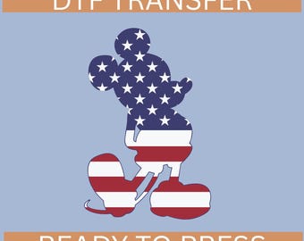 Peut inclure: Un transfert DTF avec une silhouette de Mickey Mouse remplie d'un motif du drapeau américain. Le texte "DTF TRANSFER" est en haut et "READY TO PRESS" en bas, tous deux en blanc sur fond marron.