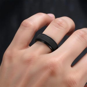 Peut inclure: Une bague noire avec une bande texturée. La bague est en acier inoxydable et a une finition mate.