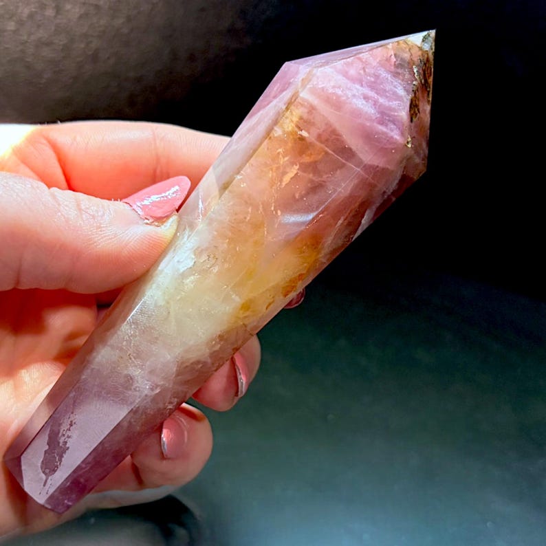 May include: A polished, hexagonal crystal point featuring a gradient of colors ranging from deep purple at the base to a translucent golden-yellow in the center and a pale, clear lavender tip with visible internal fractures and natural inclusions.