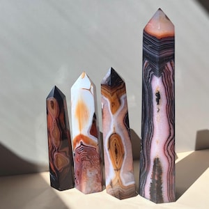 Peut inclure: Quatre tours en pierre polie de hauteurs variables disposées en rangée. Chaque tour présente des motifs en bandes distincts dans des tons de noir, blanc, brun et rose tendre, avec un sommet hexagonal pointu et une surface lisse.