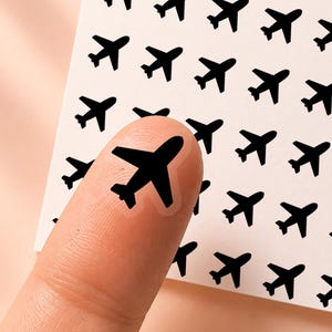 May include: A square sheet of white adhesive nail decals featuring a repeating pattern of small black airplane silhouettes. The text "honeyed sunflower" and "CL046" is printed at the top. One individual airplane decal is applied to a fingernail.