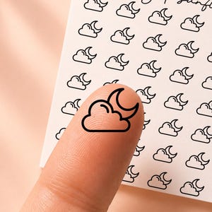 May include: A square white sticker sheet featuring a repeating black line art pattern of a crescent moon behind a cloud. The text honeyed sunflower and the code CL170 are printed in black at the top of the sheet. One sticker is placed on a finger.