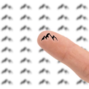 May include: A finger with a black mountain range tattoo. The background features a pattern of blurred mountain silhouettes. The image is set against a white background, creating a contrast between the finger and the design.