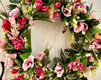 May include: A pink and green floral wreath with pink tulips and large pink flowers. The wreath is made of artificial flowers and greenery.