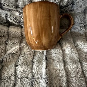 May include: A brown ceramic mug with a glossy finish. The mug has a rounded shape and a handle.
