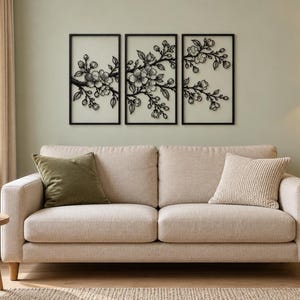 May include: A set of three rectangular black metal wall art panels featuring a detailed cutout design of flowering cherry blossom branches. Each panel is framed in black and displays a continuous botanical motif of buds and blossoms.