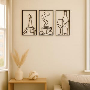 May include: Three black metal wall art pieces. The first depicts a person's legs and a book, the second a cup of coffee, and the third a wine bottle and glass. The art is displayed on a cream-coloured wall.