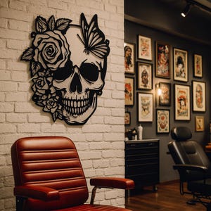 Könnte beinhalten: Schwarze Metall-Wandkunst mit einem Totenkopf-Design mit Schmetterling und floralen Akzenten. Der Totenkopf ist an einer weißen Backsteinmauer befestigt. Das Bild wurde in einem Tattoo-Studio aufgenommen.
